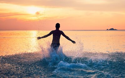 Joyful young man running in water of the tropical sea during beautiful sunset.